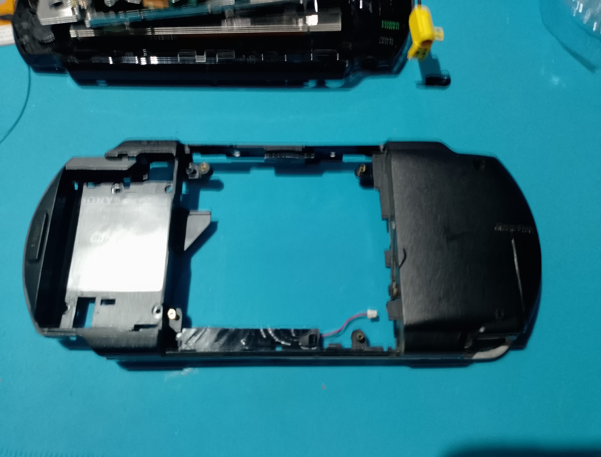 PSP-1004 замена корпуса - Задняя часть старого чёрного корпуса с UMD-зоной. Серебристое кольцо и матовый пластик выдают возраст первой PSP.