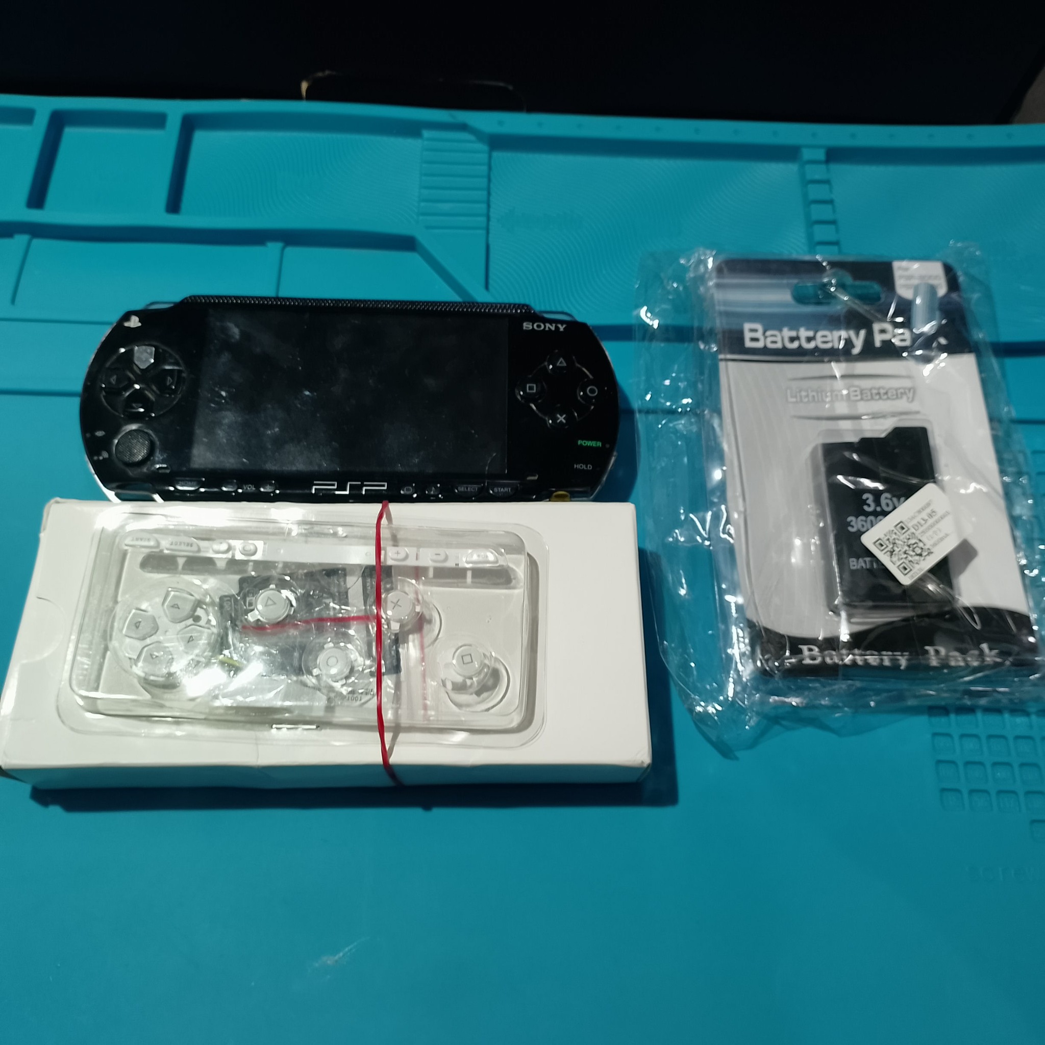 PSP-1004 замена корпуса - Перед сборкой рядом лежат чёрная PSP, белая лицевая панель и новая батарея. Так сразу видно весь план работы: корпус меняется на белый, питание обновляется.