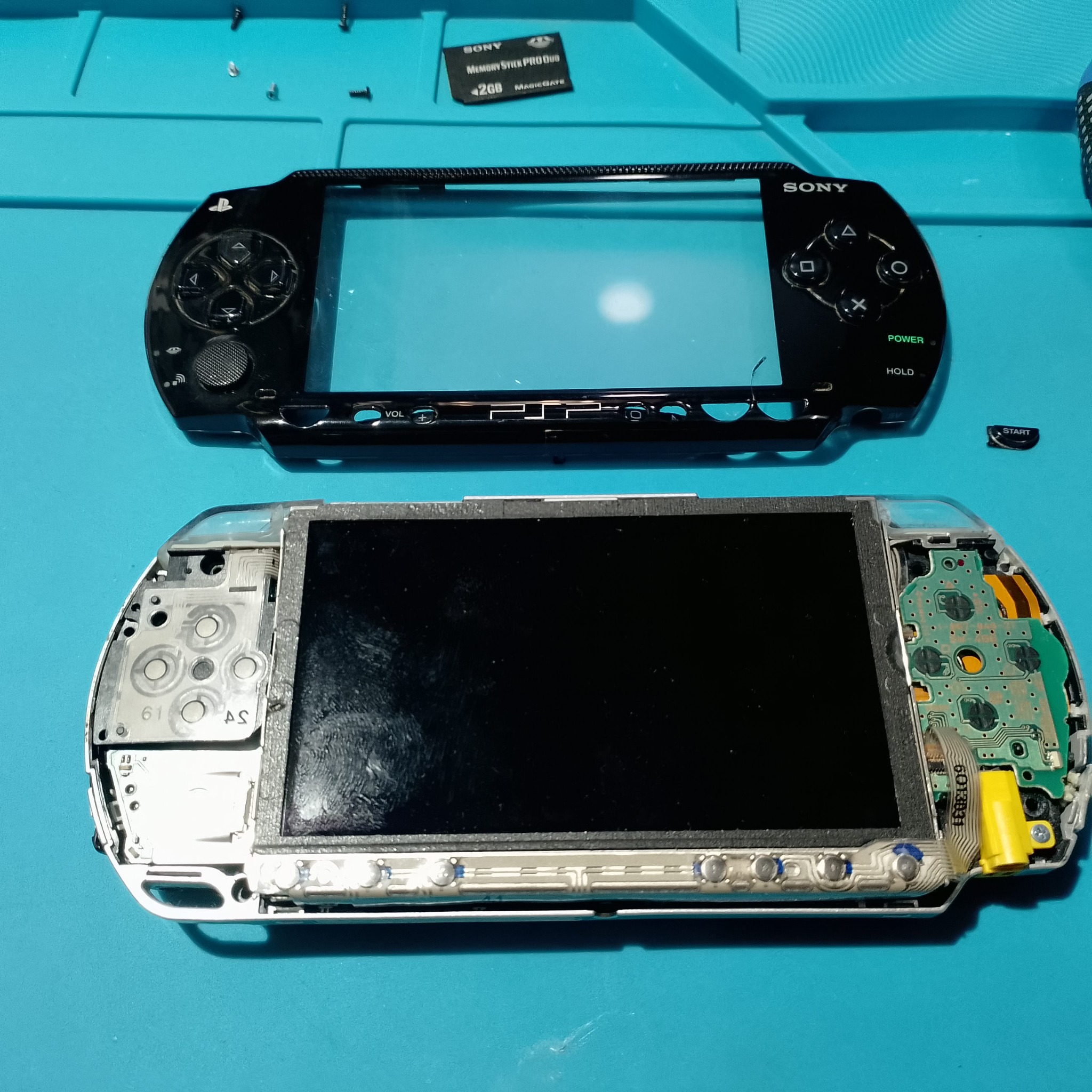 PSP-1004 замена корпуса - Лицевая панель уже снята. Старая чёрная рамка с кнопками лежит отдельно, а экран и платы кнопок открыты для чистки и примерки новой панели.
